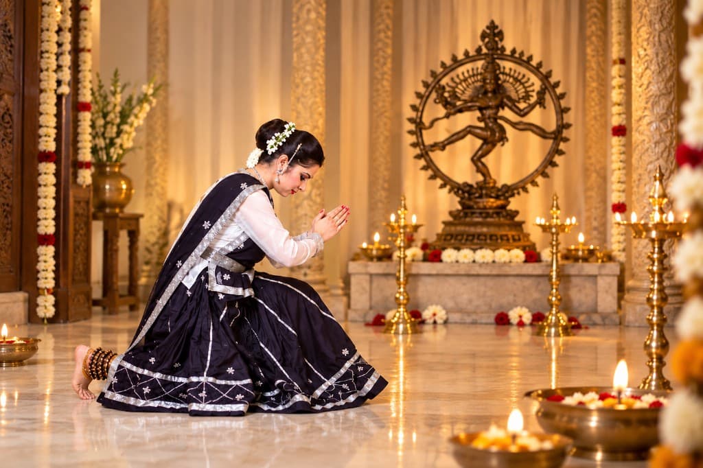 A dancer in prayer before Nataraja in a warm temple-studio setting